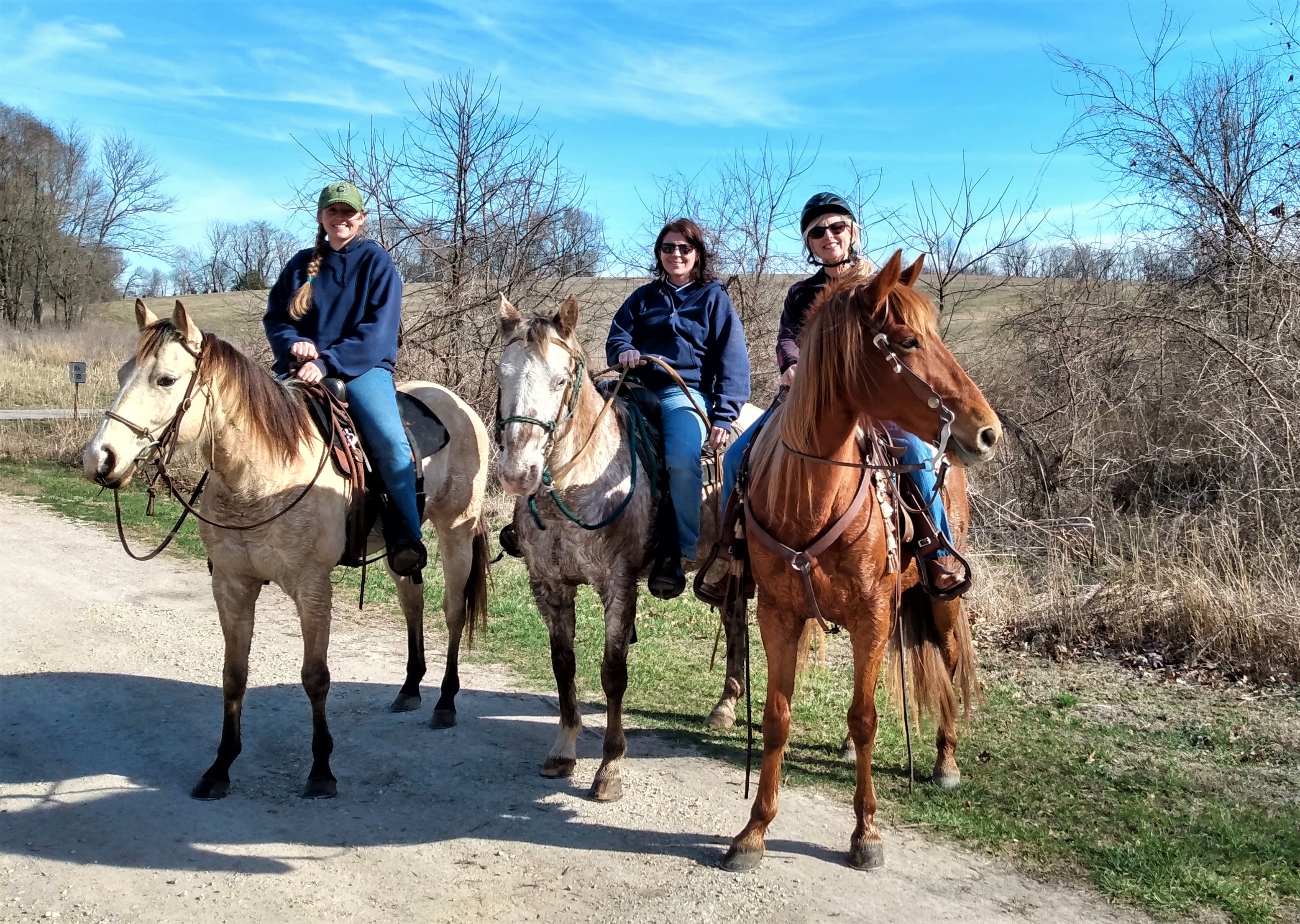 Three women ride horses on an outdoor trail near woods