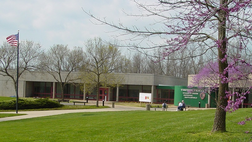 Visitors enjoy a sunny day while sitting outside the Wilson's Creek National Battlefield Visitor Center. People sit on benches outside a building