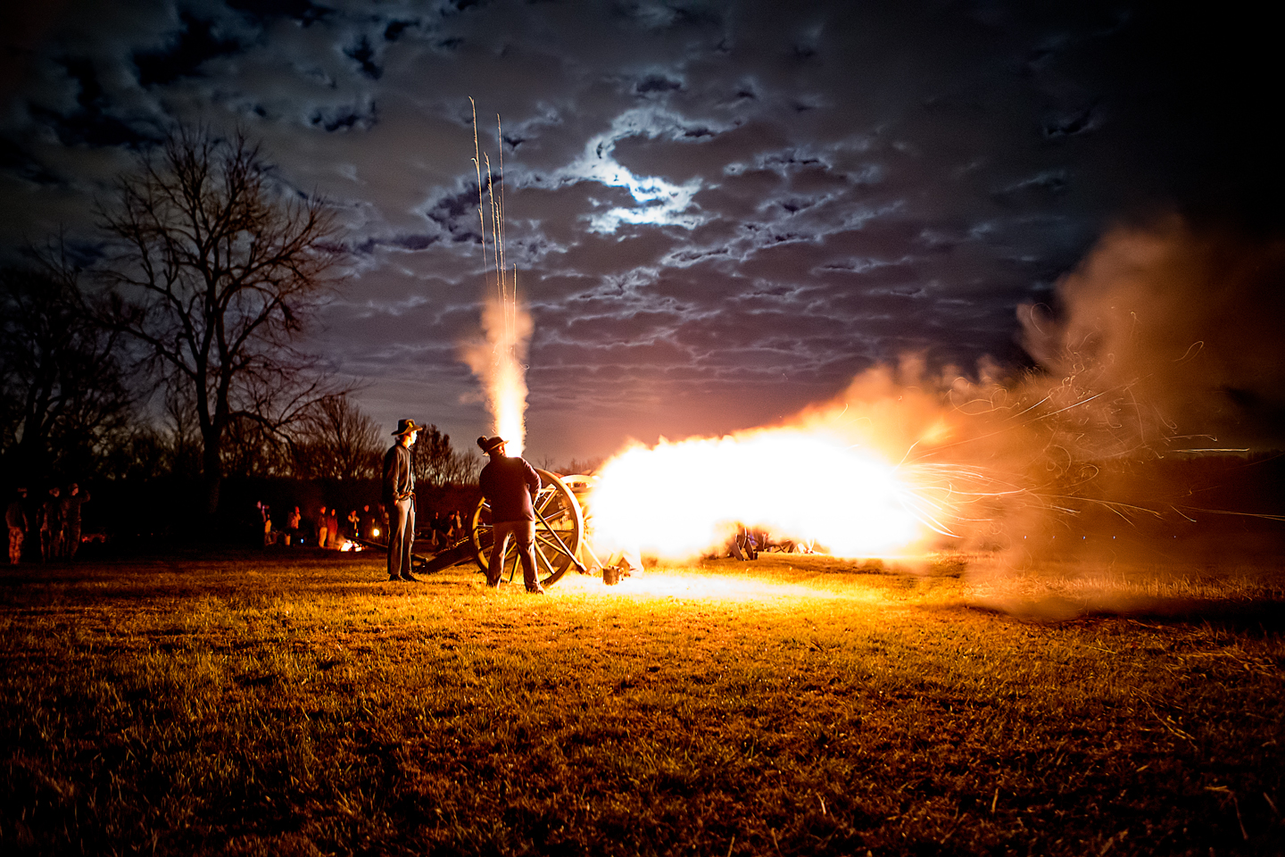 Night time artillery demonstration with orange flames brilliantly coming out of the cannons barrel and vent.