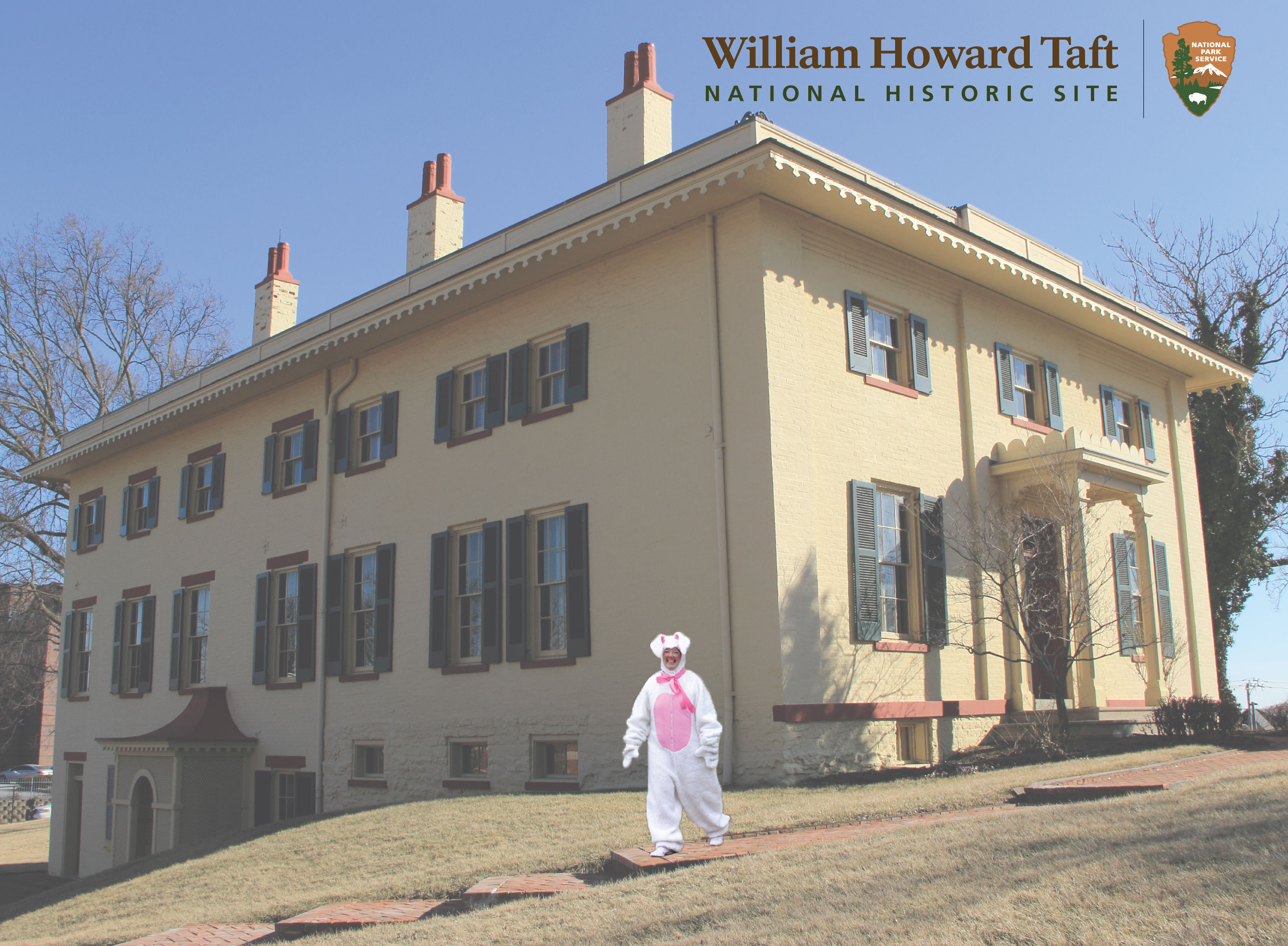 WIHO-Easter-Generic A large, two-story house with several windows on all sides and an adult in a white bunny costume walking on the sidewalk in front of the house.