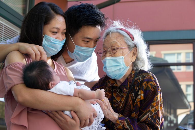 Three people wearing facemasks share an intimate moment with a newborn Three people wearing facemasks share an intimate moment with a newborn