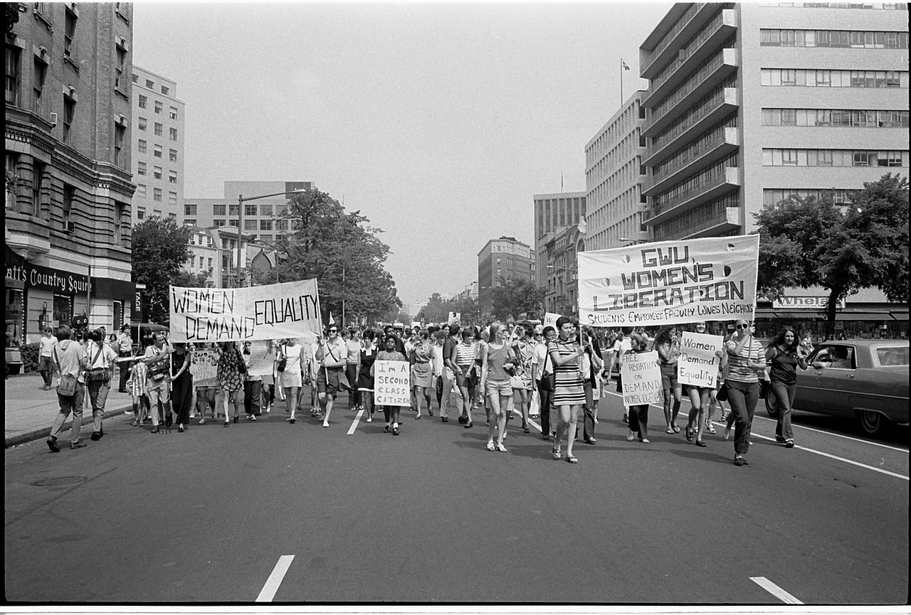 A historical photograph of the women's liberation movement with women with signs marching up a street.