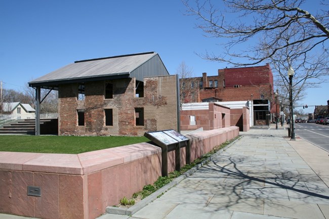 An open-air structure consisting of an assortment of red stone and brick walls and a metal roof.