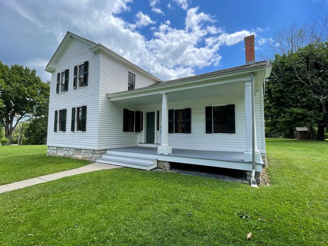 A two-story white house with a porch, seven windows with green shutters.