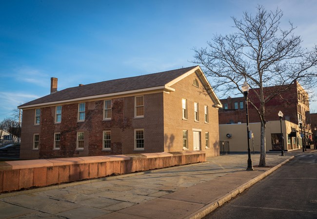 Corner view of a square, two-story, red brick building with white-trimmed windows.