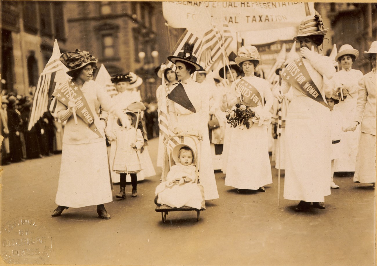 Historical photograph of women marching down a busy street in support of suffrage.