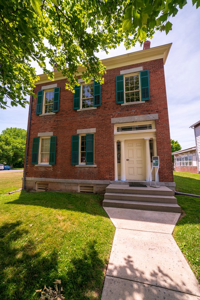 A two-story red brick building with green shutters and a white door.