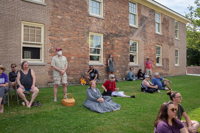 A group of people sitting in the shade of the Wesleyan Chapel wall