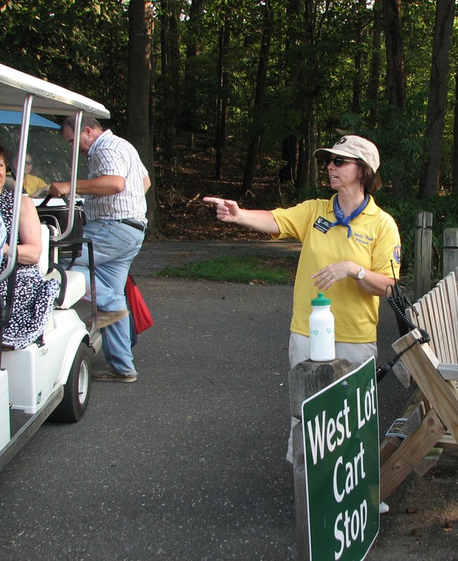 Volunteer in yellow polo points at cart for accessible ride to the Filene Center