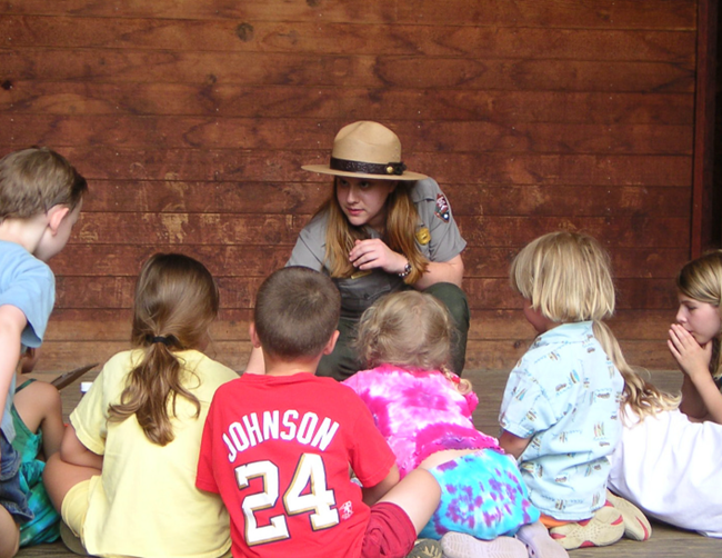 Kids with Ranger A park ranger crouches down to talk to a seated group of small childern