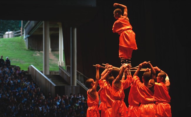 Orange clad dancers stand in a human pyramid with audience in background
