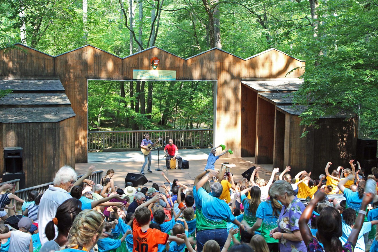A Theatre-in-the-Woods performance with artist on stage and a full audience