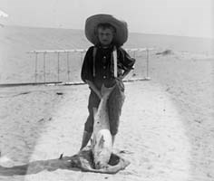 Local boy, Tom Tate, stands in front of the 1900 glider with a drum fish.