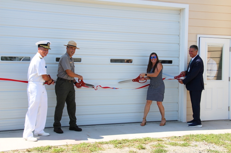 Ribbon cutting at Wright Brothers National Memorial. Four individuals cut a ribbon in front of an aviation lab building.