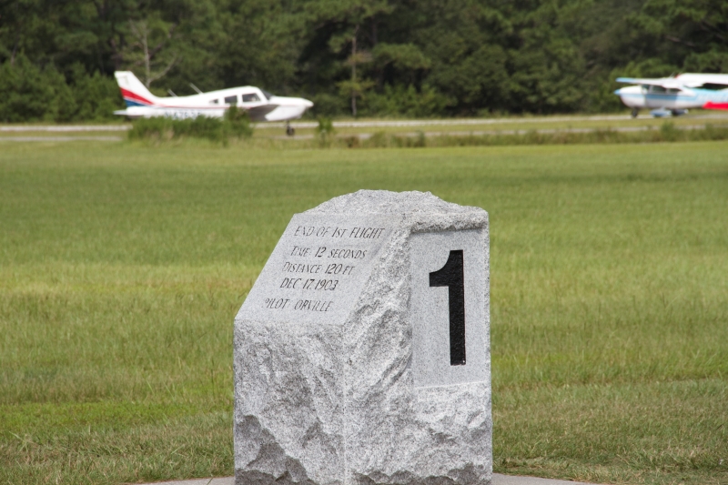 Image of the First Flight Marker and two airplanes at Wright Brothers National Memorial A granite marker in foreground and two airplanes in background.