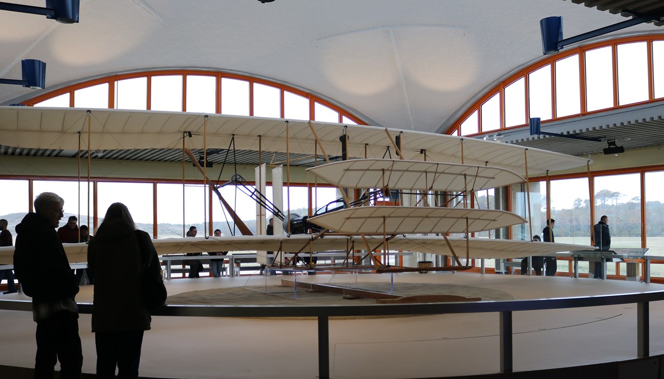 Visitors walking around reproduction of 1903 Wright Flyer inside our visitor center