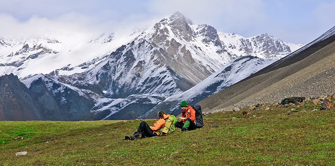 Two backpackers sitting in a high alpine meadow surrounded by mountains. Two backpackers sitting in a high alpine meadow surrounded by mountains.