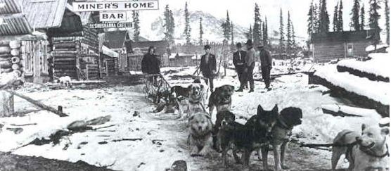 Historic photo of dog sled team with people in small town with wood buildings. Historic photo of dog sled team with people in small town with wood buildings.