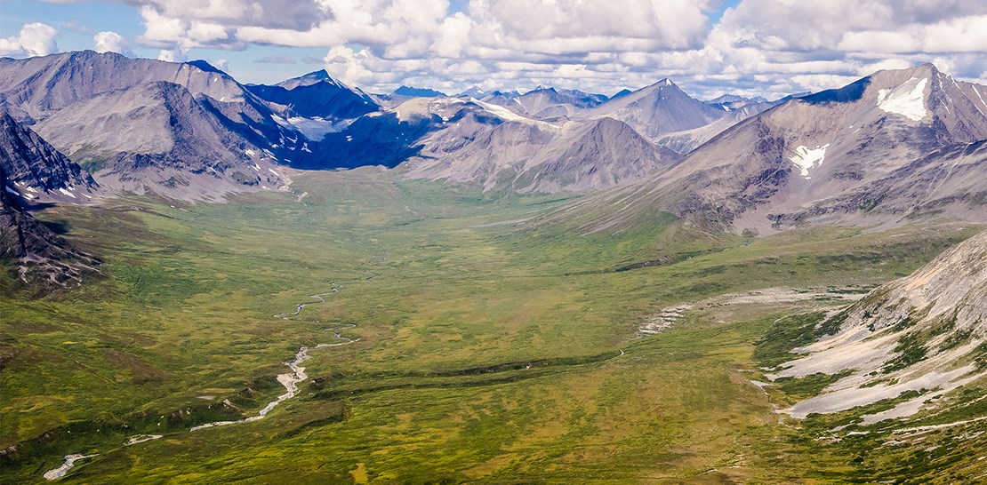 Photo of green tundra valley surrounded by rocky mountains that contain glaciers. Photo of green tundra valley surrounded by rocky mountains that contain glaciers.