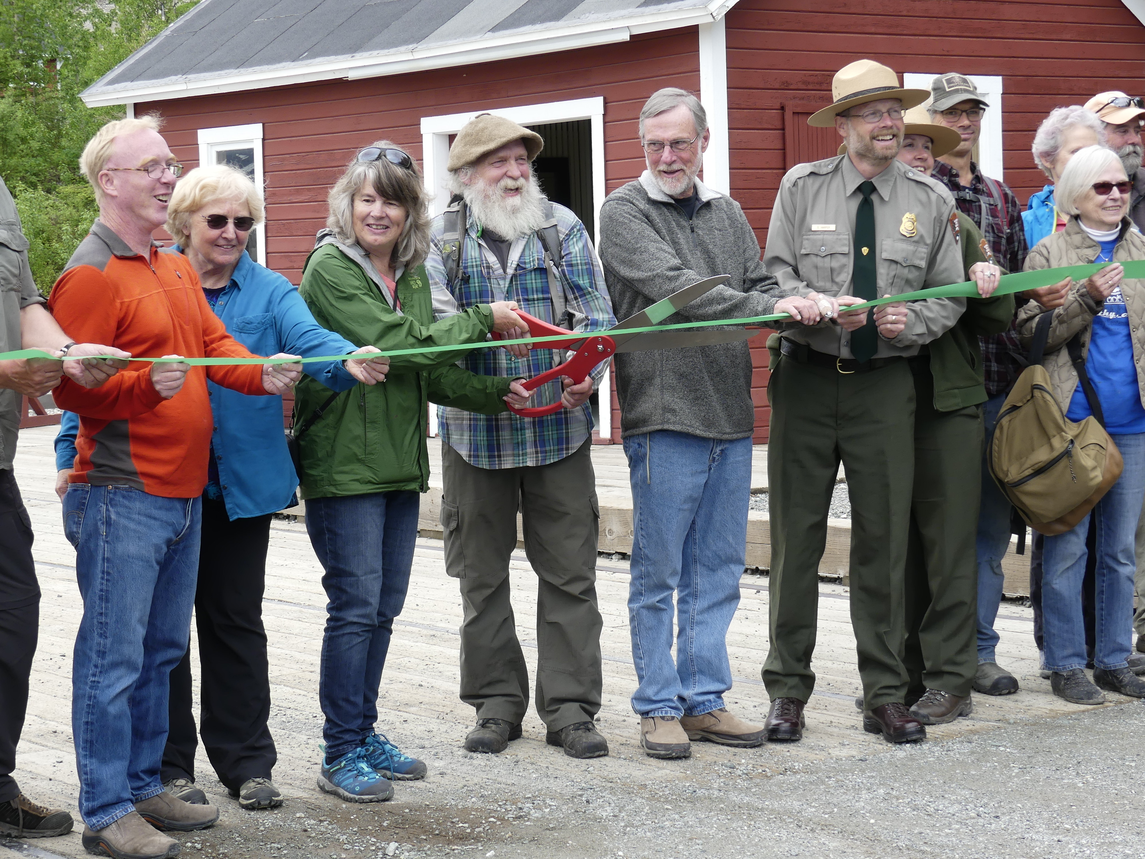 National Park Service Exhibit Specialist Carol Harding (now retired) cuts the ceremonial ribbon with the assistance of members of the McCarthy and Kennecott communities and present and former park staff.