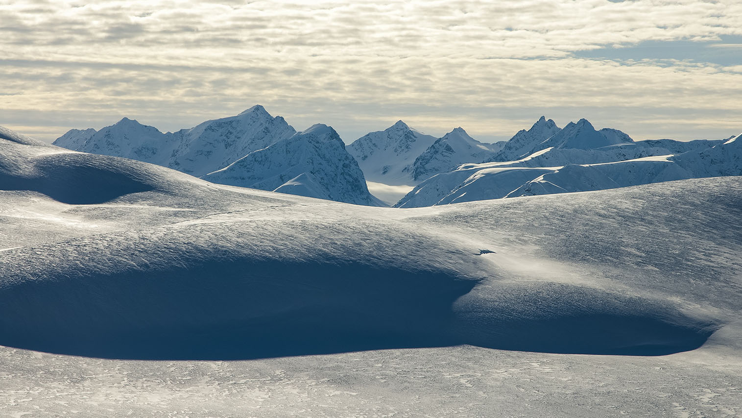Barren, snow and ice covered landscape with mountain peaks and clouds.