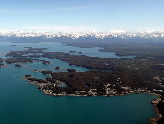 Aerial view of the town of Yakutat with forest, ocean, and islands in the foreground and snow capped mountains in the background.