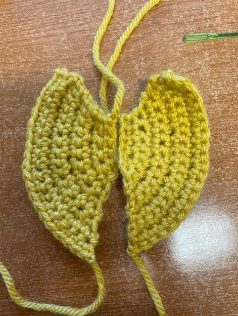 A yellow yarn crochet model of a Triops carapace which looks like wings.