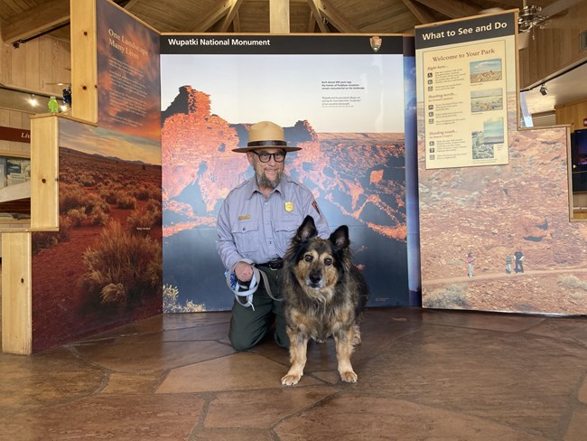 A park ranger kneels with a dog on leash in front of him