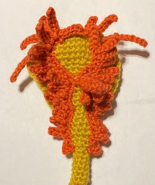 The underside of a yellow and salmon colored crochet model of a Triops showing the edopods, exopods, and gills which look like many small legs.