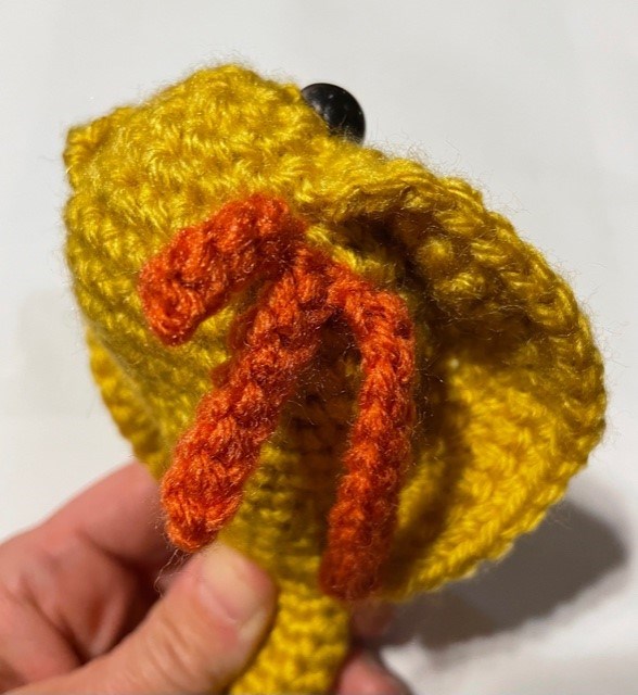 A yellow and salmon colored yarn model of a Triops being held at the bottom by a human hand.