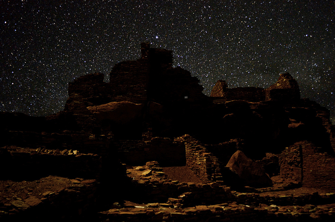 a large stone pueblo building beneath a dark sky filled with stars