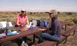 Two visitors eating lunch at a picnic table with a view of the Painted Desert.