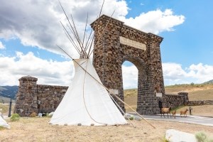 a large teepee in front of a stone archway and three elk