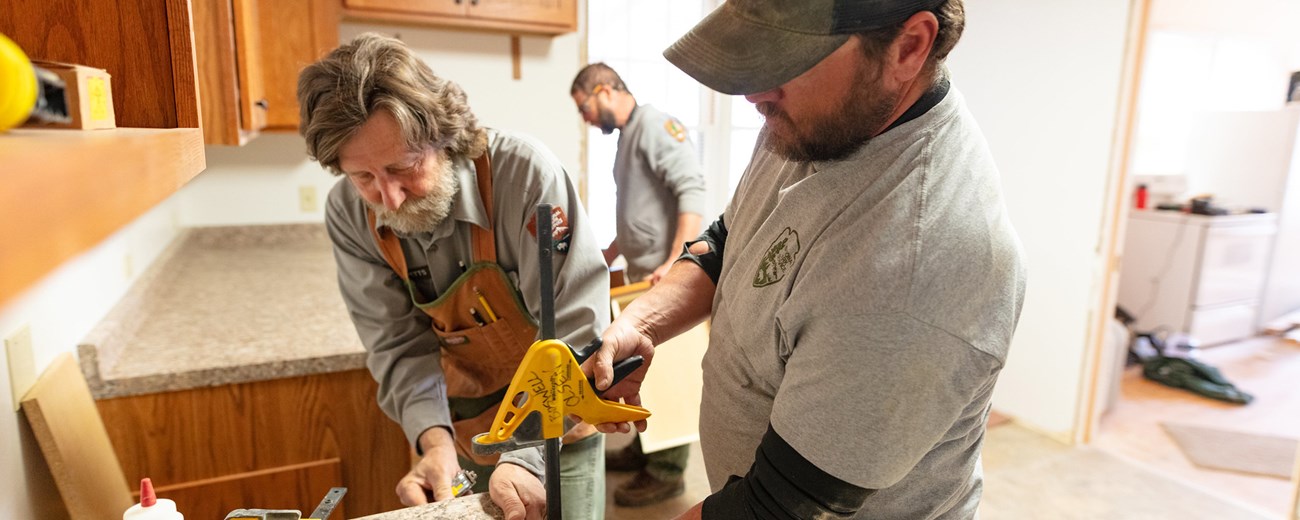 Two men hold a vice while installing a new countertop.