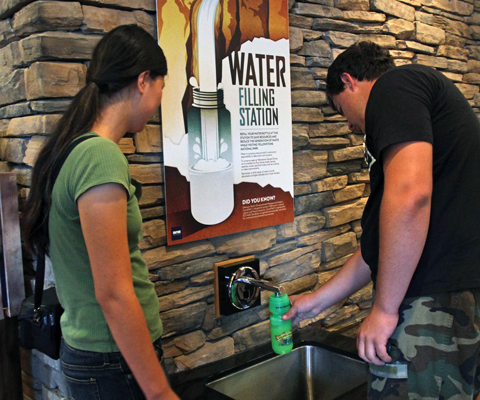 A man fills a plastic water bottle from a faucet beneath a display