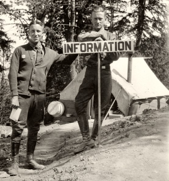 Two Yellowstone Park Rangers in front of a wooden sign that reads "Information."
