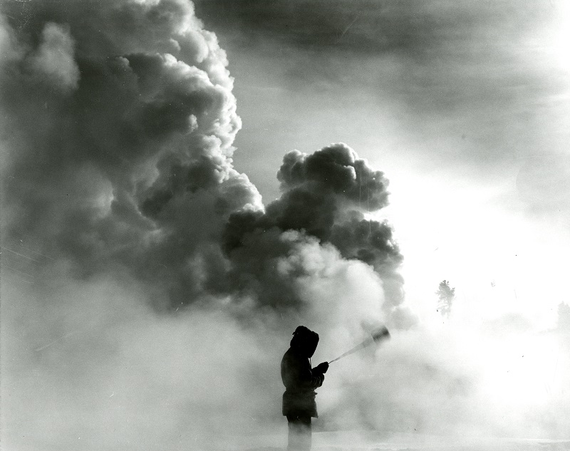 Historic black-and-white photo of a man swinging a basket, creating dramatic clouds