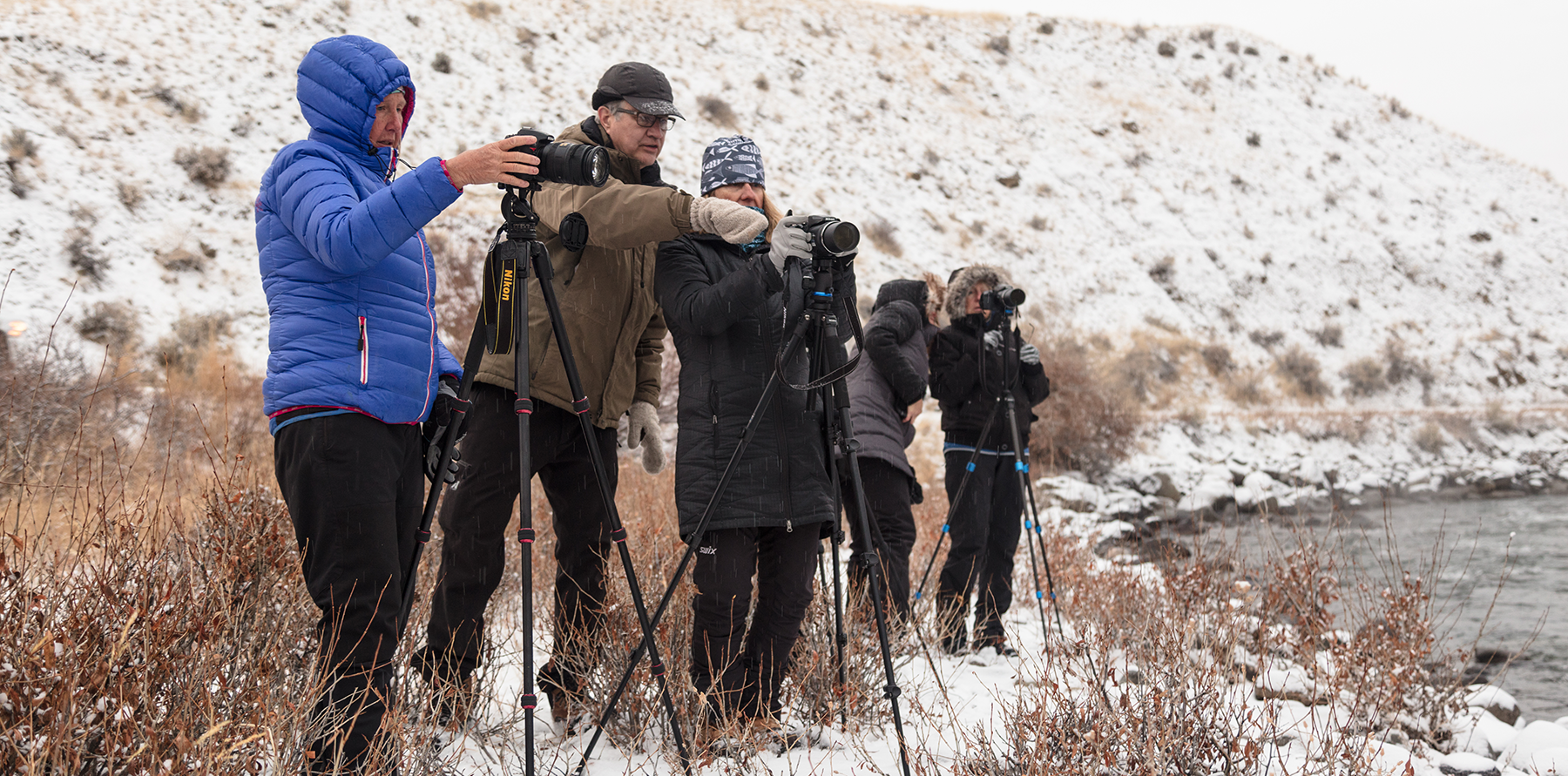 A group of adults looks through cameras on tripods while standing in the snow.