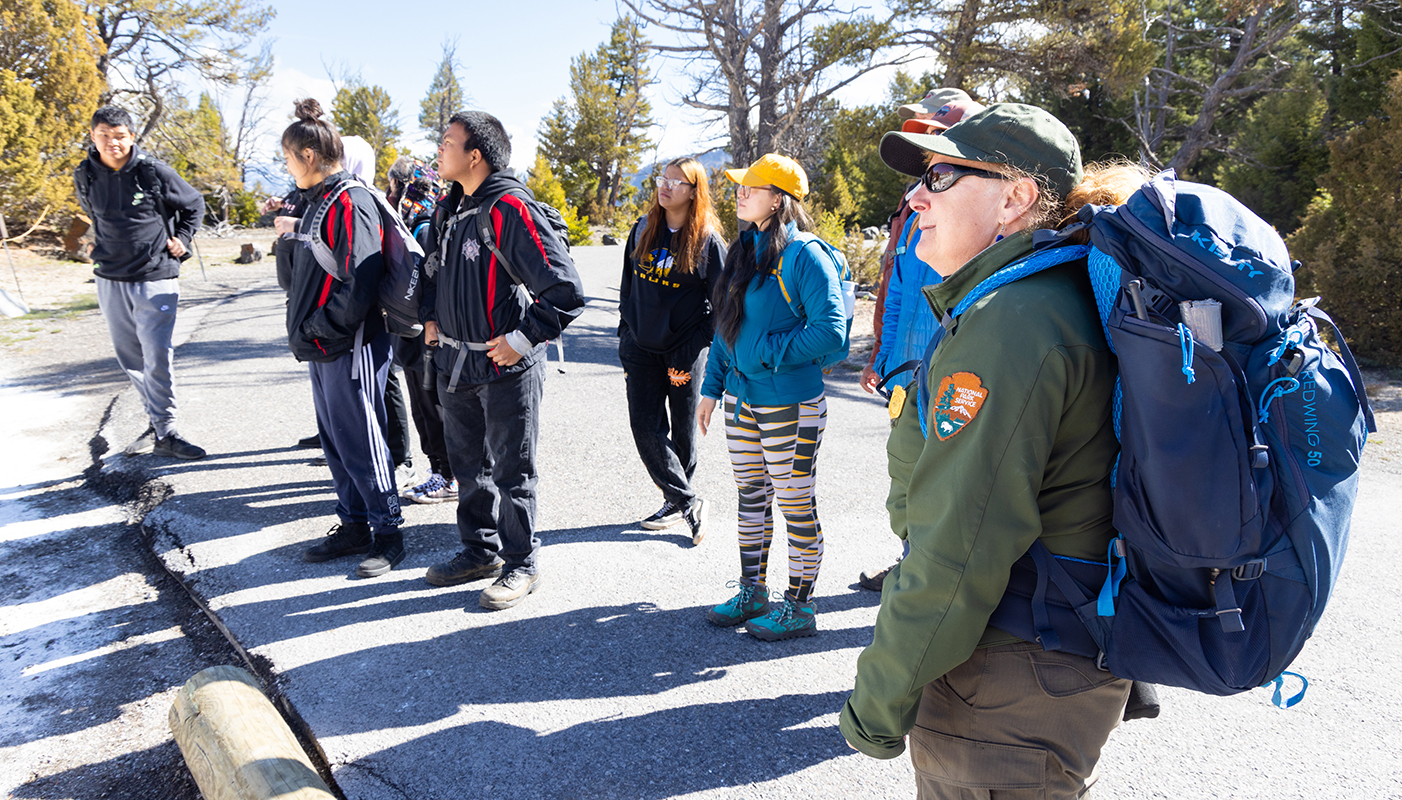 A park ranger and a class stand outside near some trees.