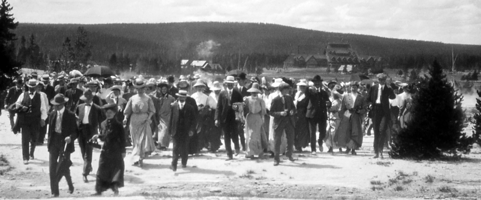 A historic photo of a large group of visitors walking away from the Old Faithful Inn A historic photo of a large group of visitors walking away from the Old Faithful Inn