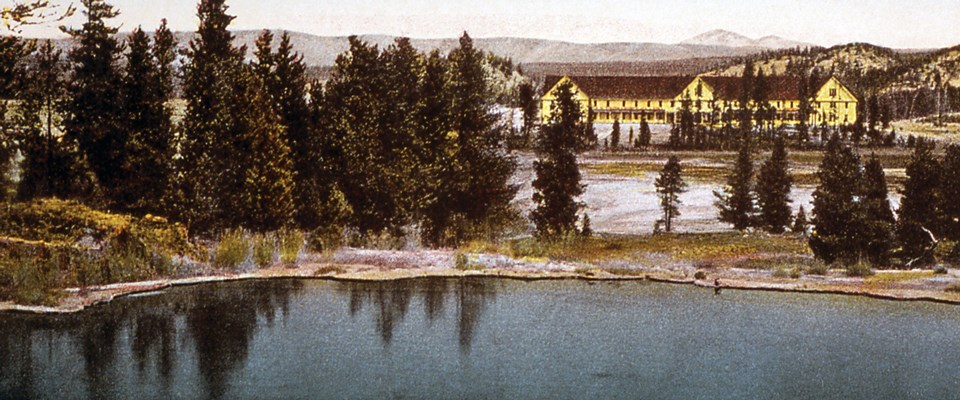 A large, yellow hotel surrounded by trees and mountains