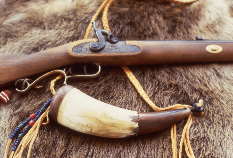 European American rifle and powder horn resting on fur.