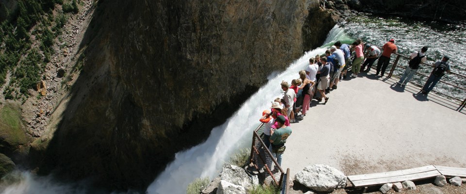 Looking down from a hill to people lining the edge of a fence overlooking a waterfall