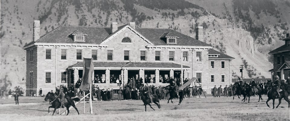 Members of the cavalry ride horses in front of a sturdy stone building