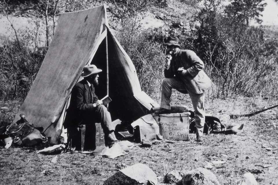 An historical photo of two men talking in front of a canvas tent.
