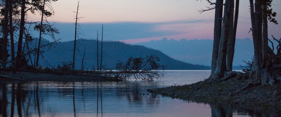 Calm waters reflect trees and mountains Calm waters reflect trees and mountains