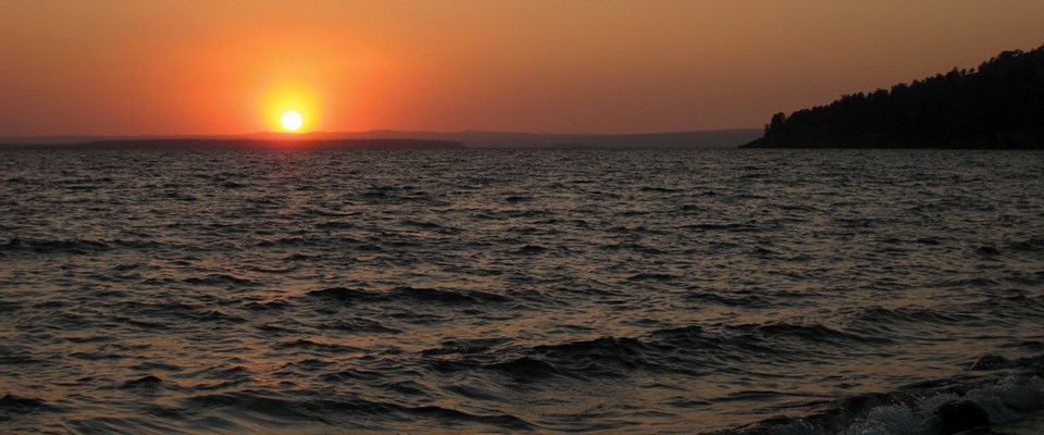 Sunset on a large lake with rock outcropping covered in trees