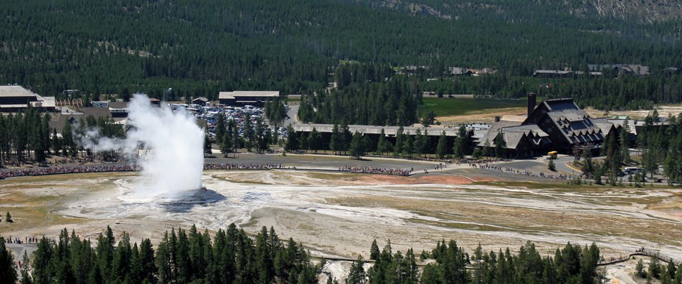 An aerial view of bleachers for viewing Old Faithful, the geyser erupting, the inn and lodge, and other buildings