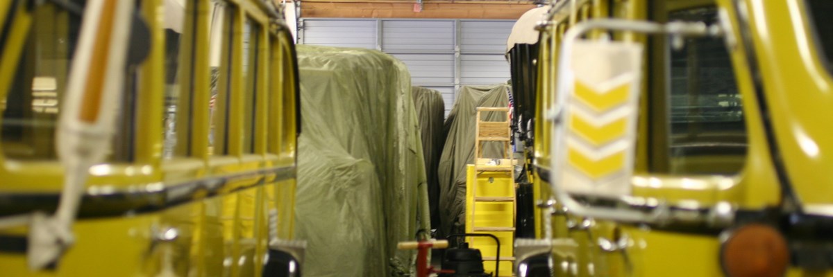 Yellow historic vehicles at the front of a line of vehicles covered in drapes in a garage