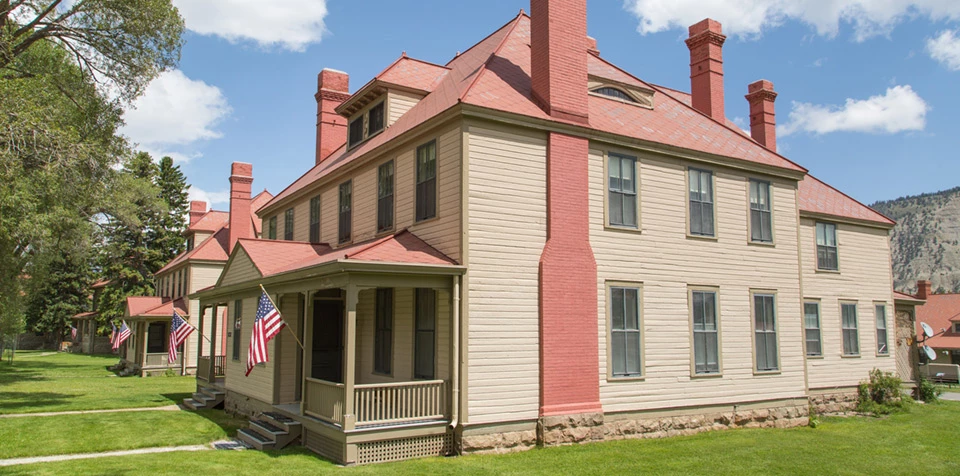 Fort Yellowstone Officer's Quarters A row of three story buildings with wood siding, red roofs, and tall brick chimneys.